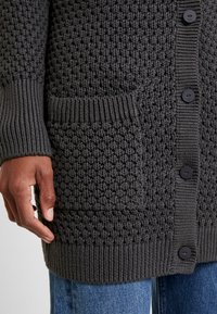 Cardigan lavorato a maglia grigio scuro con un motivo strutturato, polsini a coste e una tasca singola, dettagliato con bottoni neri.