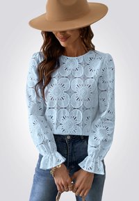 Top de encaje azul claro con diseño de recortes florales, mangas largas abullonadas y puños acampanados, combinado con unos jeans de mezclilla oscura.