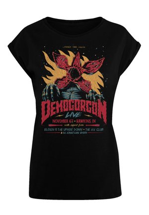 Schwarzes T-Shirt mit einem Grafikdruck eines roten Blumenmotivs und Demogorgon, mit mehrfarbigem Text, der eine Live-Veranstaltung im November ankündigt.