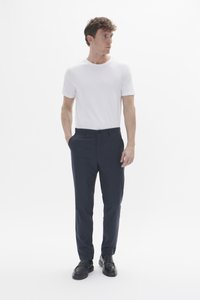 Camiseta blanca de manga corta combinada con pantalones de vestir azul marino. Los pantalones cuentan con bolsillos laterales y una textura suave; se llevan con mocasines negros.