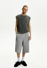Top in maglia grigia a maniche corte con trama, pantaloni corti grigi larghi con coulisse, calze bianche alla caviglia, scarpe in suede nere, design minimalista contro uno sfondo neutro.