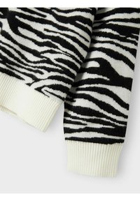 Tessuto a maglia con motivo zebra in bianco e nero, con polsini a coste e una texture morbida. Il design presenta strisce audaci di larghezze variabili.
