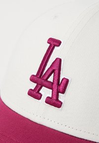 Burgundi és fehér baseball sapka, az elején hímzett "LA" logóval. A felső része fehér, a napernyő burgundi színű.