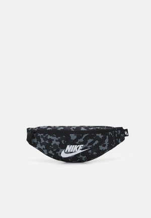 Sac banane Nike camouflage noir et gris avec logo blanc et fermeture éclair sur un fond uni clair.