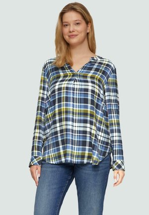 Langsleeve, v-hals-shirt in een blauw, groen en wit geruit patroon. Gemaakt van zacht materiaal met een relaxte pasvorm en zijsplitten. Gecombineerd met blauwe jeans.