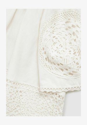 Weißer Stoff mit filigraner Spitze, die florale Muster und geometrische Formen entlang der Kanten zeigt, und eine zarte Textur hervorhebt.