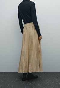 Kreemi pleediga maksiseelik, mis on valmistatud kergest kangast ja millel on seotav vöökoht. Komplektis tume pika varrukaga topp ja mustad kingad.