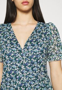 Květinové šaty s kratšími nabíranými rukávy, V-výstřihem a navy podkladem s modrými a bílými květinovými vzory. Měkká, lehká tkanina.