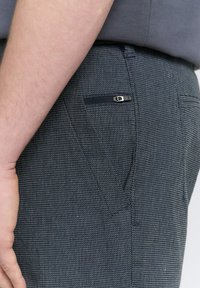 Marineblaue gewobene Hose mit strukturierten Oberflächen, ausgestattet mit einer Reißverschluss-Tasche auf der rechten Seite. Eng anliegend mit geradem Schnitt.