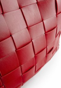 Primer plano de tiras de cuero rojo entrelazadas en un patrón de tablero de ajedrez texturizado en una bolsa o accesorio.