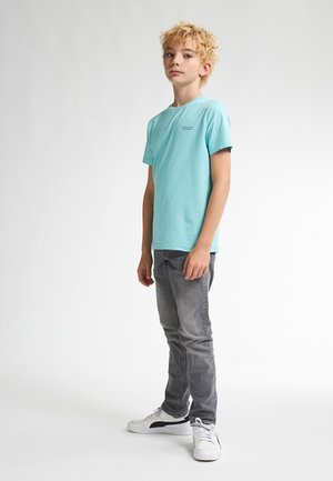 Camiseta de algodón azul claro con manga corta y cuello redondo, combinada con jeans gris ajustados y zapatillas blancas.