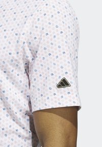 Kortærmet skjorte i hvid med håndtegnet mønster i pink og blå. Har et sort Adidas-logo på ærmet. Blødt, lette materiale.