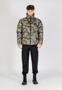 Maskovací péřová bunda s vysokým límcem, zapínáním na zip a nášivkou s logem. Sladěná s černými cargo kalhotami a černými šněrovacími botami.