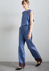 Modra vzorirana brezrokavnik in ujemajoče se hlače z maroon poudarki na robu. Tkanina, podobna svili, ohlapen kroj in geometrijski vzorec.