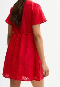 Czerwona lniana sukienka z krótkimi rękawami, wzorem w dziurki, regulowanym paskiem w talii i rozkloszowanym dołem, prezentująca teksturowany materiał.