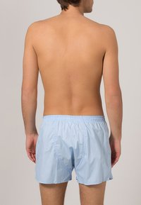 Ljusblå badshorts med ett elastiskt midjeband, tillverkade av mjukt tyg, med en avslappnad passform och sidofickor.