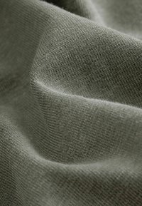 Tissu texturé dans un vert doux, mettant en valeur de fins motifs tricotés et des fibres douces. Le matériau semble lisse avec de légers plis.