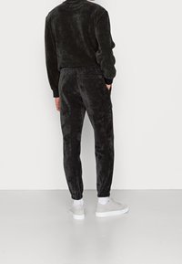 Tuta in velluto nero con vestibilità comoda. La parte superiore presenta un collo e polsini a coste, mentre i pantaloni hanno polsini elasticizzati e tasche laterali.