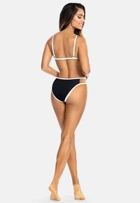 Zestaw bikini z czarną bazą i białym wykończeniem. Góra ma cienkie ramiączka i prosty design, podczas gdy dół posiada akcenty w formie wycięć.