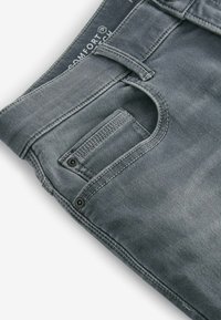 Szare dżinsy z zamkiem błyskawicznym i guzikiem, przednią kieszenią oraz kontrastowym przeszyciem wzdłuż szwów. Miękka faktura i swobodny design.