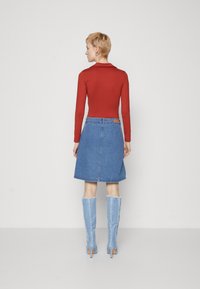 Czerwona, długa bluzka z długim rękawem w połączeniu z niebieską spódnicą w kształcie litery A z denimu. Niebieskie botki do kolan z postrzępionym detalem. Jednolite kolory, casualowy design.
