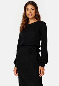 Maglione nero a coste con maniche lunghe e design aderente, dotato di una cintura legata in vita per un tocco in più.