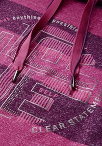 Sweatshirt fuchsia en tissu texturé, avec de grands motifs graphiques et des phrases violettes. Comprend des cordons assortis avec des embouts métalliques.