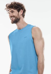 Ljusblå ärmlös bomullstopp med rund halsringning och en diskret logotyp på bröstet. Slät textur och avslappnad passform.