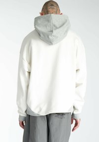 Hvid sweatshirt med grå hætte og ribbede manchetter, med en løs pasform og afrundet kant. Inkluderer synlige sømdetaljer.