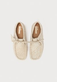 Beige textúrájú cipők, fűzős masnival, puha anyagból, lapos talppal és kerek orral, belsejében "Clarks ORIGINALS" felirattal.