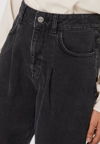 Höga svarta denimjeans med synlig sömnad, en framficka och silverknappstängning. Tjockt tyg med en lätt textur.