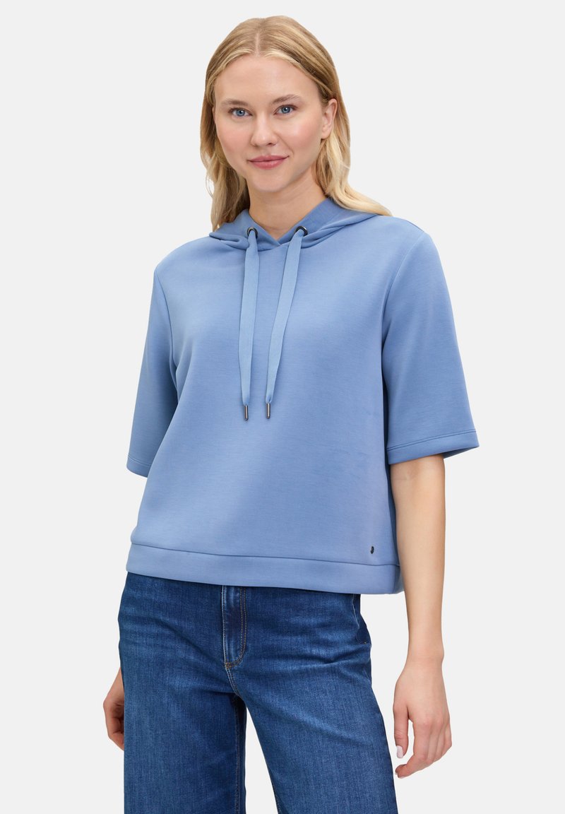 Jasnoniebieska, krótkozasięgowa bluza z kapturem, z sznurkiem, gładka w dotyku i luźna. Połączona z ciemnoniebieskimi dżinsami.