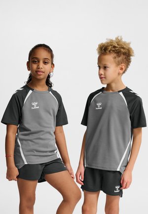 Dos niños están de pie mirando hacia adelante, vestidos con ropa deportiva a juego en gris y negro con detalles blancos y logos de "hummel".