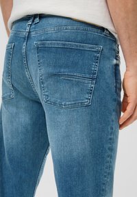 Blauwe denim jeans met een rechte snit, twee achterzakken en een gladde textuur. De stof vert toont subtiele vervaging en whiskering-details.