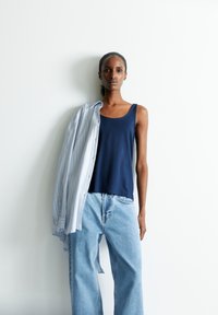 Marine tanktop, lichtblauw gestreept hemd over de schouders gedrapeerd, en losvallende lichtblauwe spijkerbroek. Gladde stof, casual ontwerp.