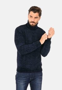 Maglione a collo alto blu navy in un pattern a maglia testurizzata. Presenta polsini e orlo a coste, abbinato a jeans di denim.