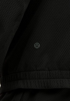 Crna sportska jakna od teksturirane mrežaste tkanine. Na donjem rubu ističe se prepoznatljiv logotip. Jednostavan dizajn, funkcionalan kroj.