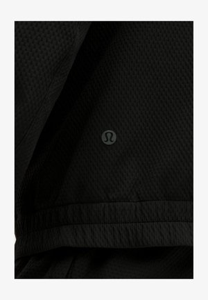 Chaqueta deportiva negra con tejido de malla texturizado. Presenta un logo distintivo en el bajo. Diseño simple, corte funcional.