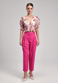 Blumenbluse mit Puffärmeln in Hellrosa, verziert mit roten und gelben Blumen, kombiniert mit hochtaillierten, leuchtend pinken Hosen und cremefarbenen Absätzen.