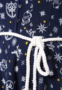 Marineblaues Kleid mit maritimen Druck, weißem Taillengürtel, Knopfverschluss und dekorativen Sternen. Weicher Stoff mit Musterdesign.