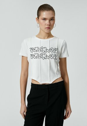 Camiseta corta blanca con texto gráfico negro "SIN MIEDO". Material de algodón, mangas cortas y costuras verticales crean un diseño estructurado.