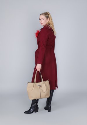 Cappotto in lana bordeaux con una decorativa piuma rossa, abbinato a stivali neri sopra il ginocchio e una borsa beige con accenti in catena.