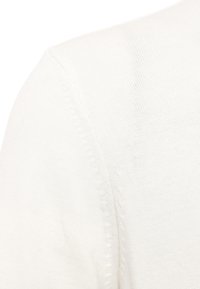 Valkoinen neulottu villapaita, joka on sileä ja pehmeä, V-pääntiellä ja näkyvillä saumoilla. Kevyt ja pehmeä materiaali.