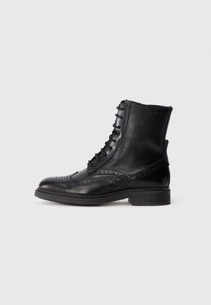 Black leather lace-up ankle boot with brogue detailing and low stacked heel, side zipper, and subtle brand logo near the top.