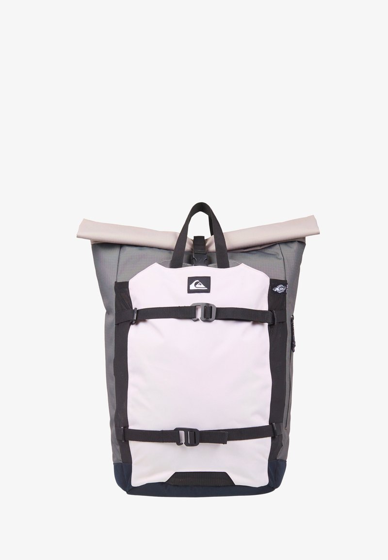 Sac à dos à rabat roulé gris et beige avec des bretelles noires réglables et une poche avant affichant un petit logo de montagne.