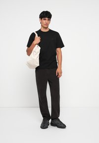 Black cotton t-shirt with short sleeves, paired with dark corduroy pants and black sneakers. Model carries a light beige tote bag.