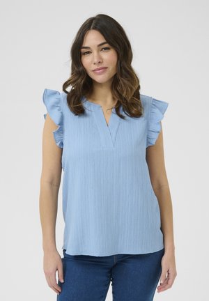 Haut bleu clair à manches courtes avec détails en volants, en tissu texturé, et un design en V. Porté sur un jean bleu ajusté.