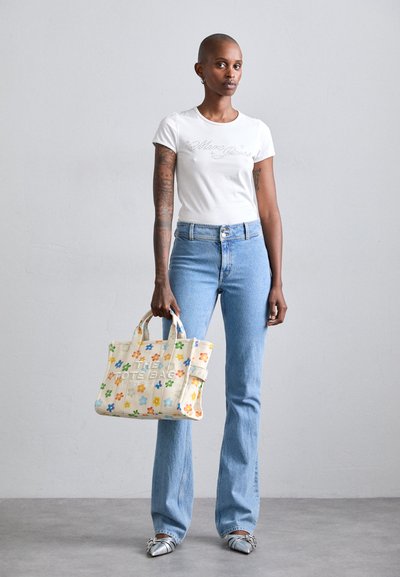 Tote bag laget av lerret, med flerfargede blomsterdesign. Hvit t-skjorte og blå utsvingte jeans kombinert med sølvfargede spisse sko.