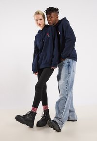 Ναυτικές φούτερ με μπροστινή τσέπη, διακοσμημένα με κόκκινο κεντητό σχέδιο. Μαύρες πλατφό�ρμες, σε συνδυασμό με μαύρα κολάν και φθαρμένα τζιν.