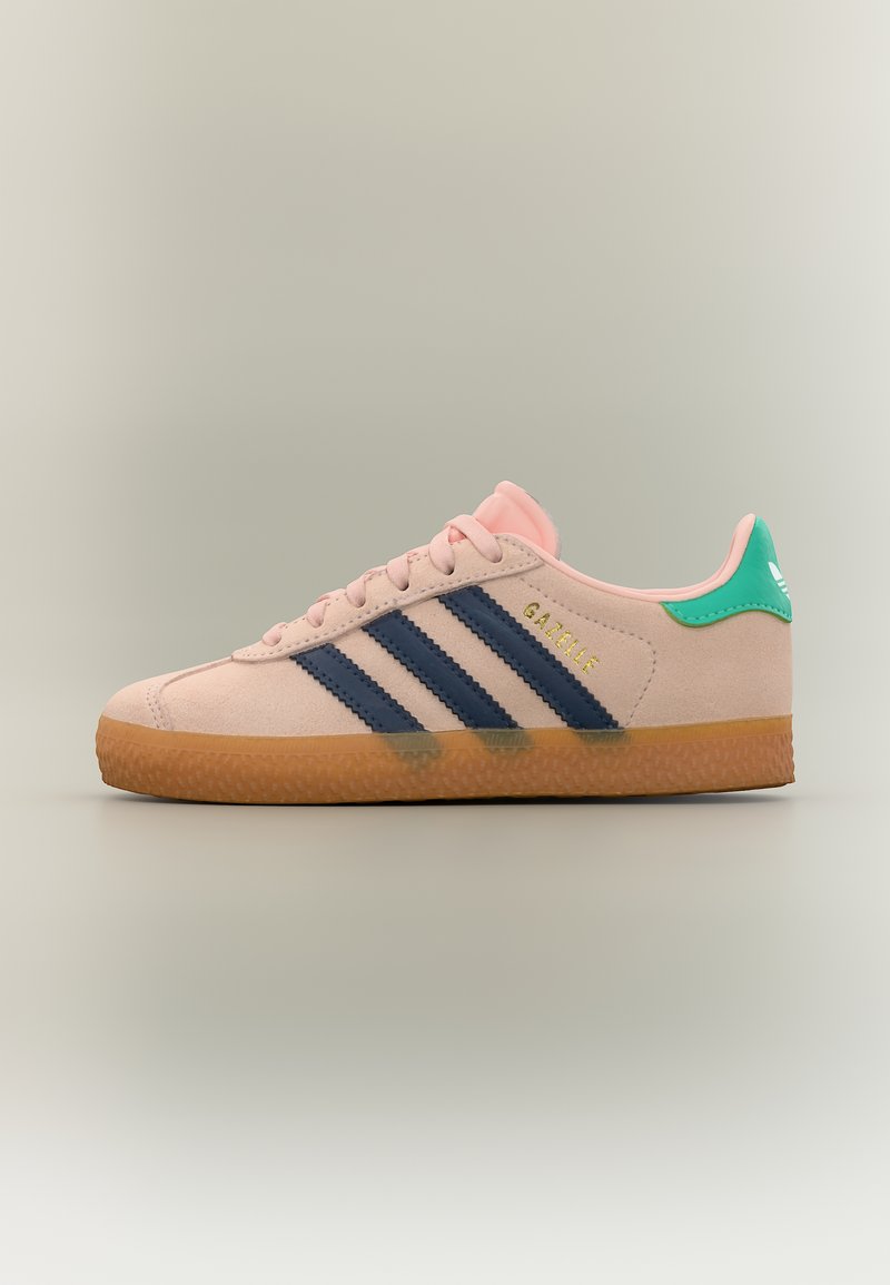 Απαλό ροζ αθλητικό παπούτσι Adidas Gazelle με ναυτικό μπλε ρίγες, πράσινη ετικέτα στη φτέρνα, καουτσούκ σόλα και χρυσό κείμενο "GAZELLE" στο πλάι.